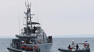 file photo, migrants stand aboard a Cyprus marine police patrol boat as they are brought to harbour