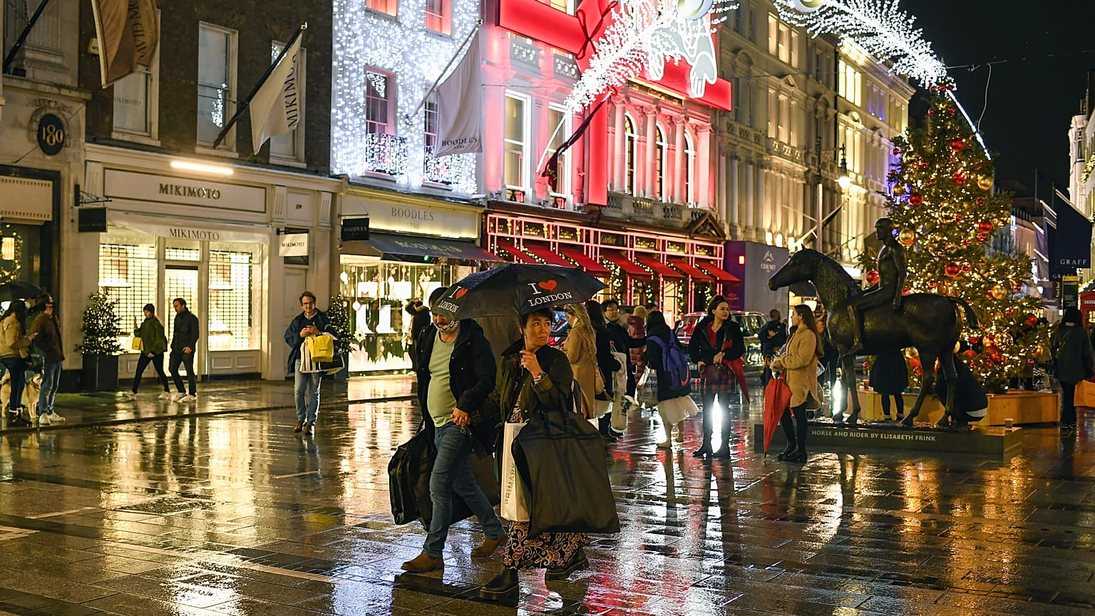A couple cross the road as they carry an umbrella and shopping bags, in Mayfair, December 19. 2020.