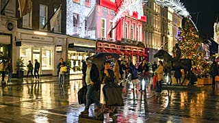 A couple cross the road as they carry an umbrella and shopping bags, in Mayfair, December 19. 2020.