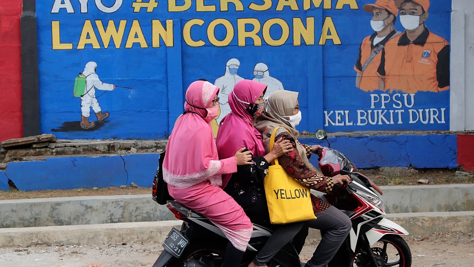 Muslim women ride a motorbike past a coronavirus-themed mural in Jakarta, Indonesia, Thursday, Sept. 10, 2020. Writings on the mural read "Let's fight coronavirus together"