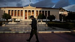 A man wearing a protective mask to curb the spread of the coronavirus walks in front of the Athens University building