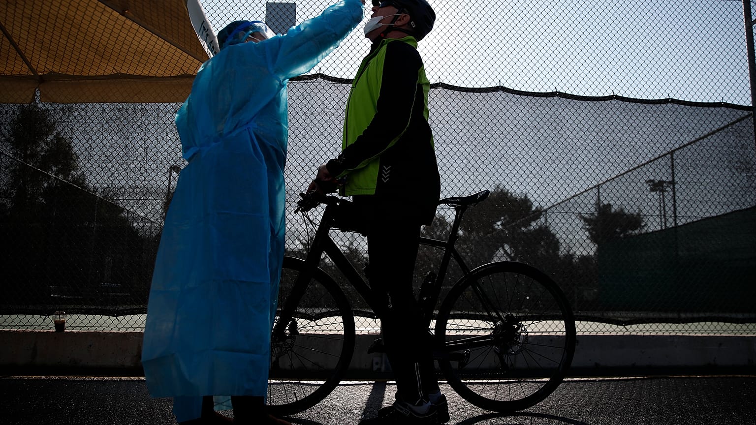 A medical staff member of the National Health Organization (EODY) conducts a COVID-19 rapid test on a bicycle rider at a drive-through testing site in Athens