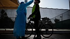 A medical staff member of the National Health Organization (EODY) conducts a COVID-19 rapid test on a bicycle rider at a drive-through testing site in Athens