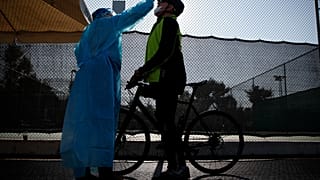 A medical staff member of the National Health Organization (EODY) conducts a COVID-19 rapid test on a bicycle rider at a drive-through testing site in Athens
