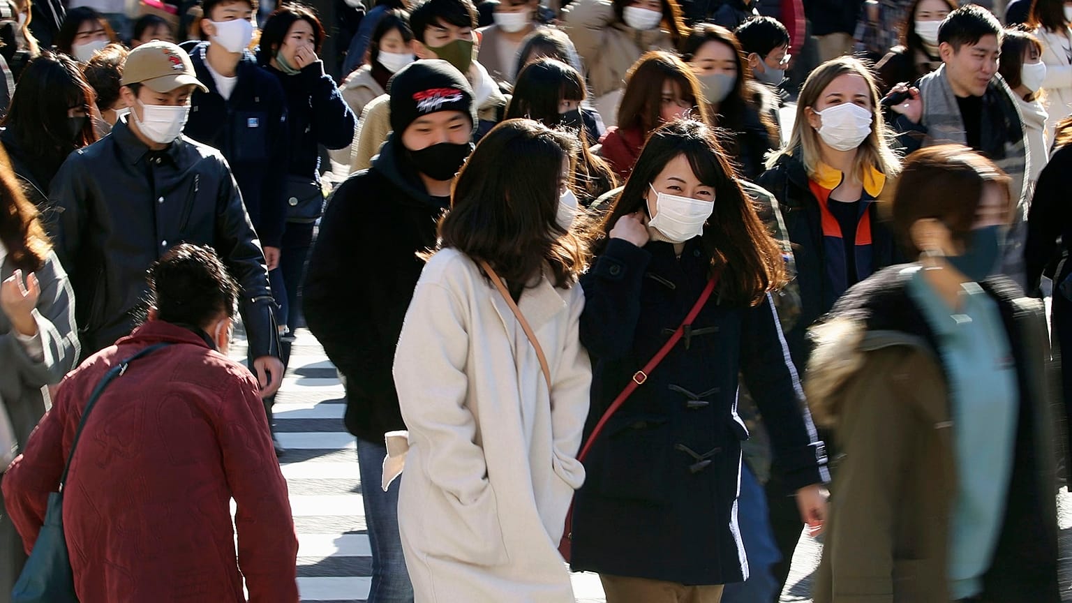 People wearing face masks to help curb the spread of the coronavirus walk around the scrambled intersection at the Shibuya shopping district in Tokyo Saturday, Dec. 26, 2020.