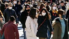 People wearing face masks to help curb the spread of the coronavirus walk around the scrambled intersection at the Shibuya shopping district in Tokyo Saturday, Dec. 26, 2020.