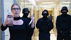 Ljubov Szobol a korrupcióellenes alapítvány irodai folyosóján, mögötte rendőrökkel, 2019-ben