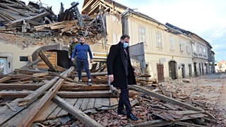 People move through remains of a building damaged in an earthquake, in Petrinja, Croatia, Tuesday, Dec. 29, 2020.