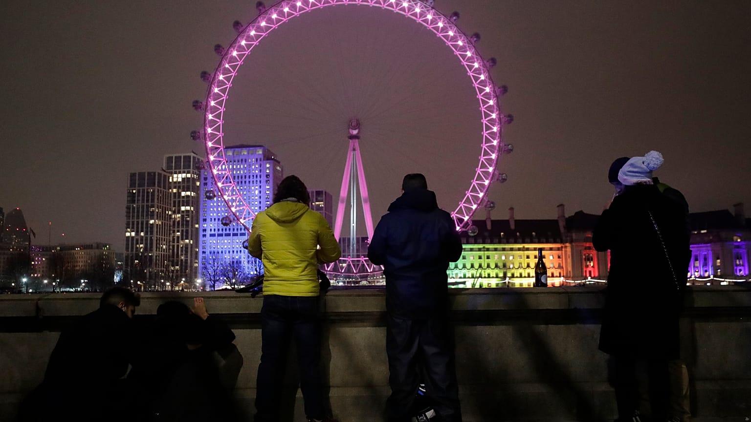 A small group of people look across from the embankment towards the London Eye ferris wheel by the River Thames in London as the New Year starts in London, Friday, Jan 1, 2021