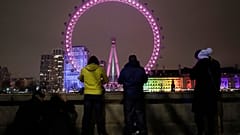 A small group of people look across from the embankment towards the London Eye ferris wheel by the River Thames in London as the New Year starts in London, Friday, Jan 1, 2021
