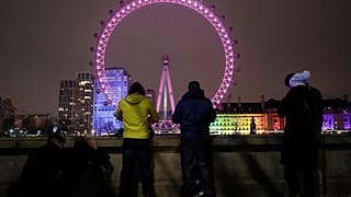 A small group of people look across from the embankment towards the London Eye ferris wheel by the River Thames in London as the New Year starts in London, Friday, Jan 1, 2021