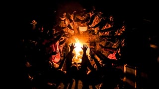 Migrants stretch their hands above a fire at the Lipa camp outside Bihac, Bosnia, Wednesday, Dec. 30, 2020, after hundreds failed to be relocated from the burnt-out tent camp.