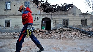 A rescuer walks past a building damaged in Petrinja.