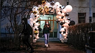 Children stand in the doorway of an apartment building, framed by a a new year's balloon decoration in Bucharest, Romania, Friday, Jan. 1, 2021. 