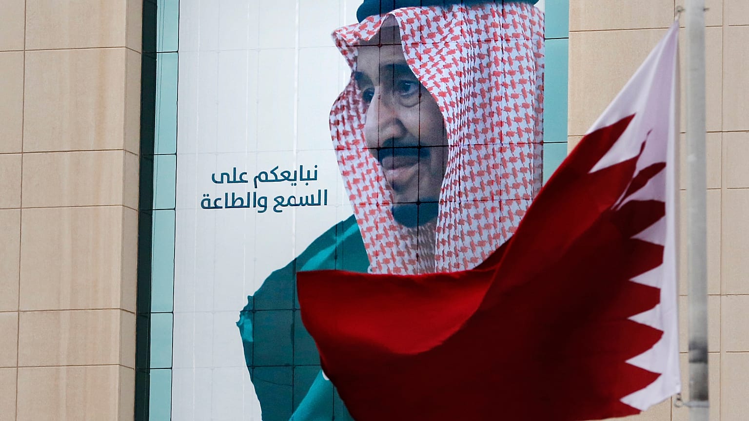 علم قطري يرفرف أمام لافتة تظهر الملك السعودي سلمان في مركز تجاري في الرياض، المملكة العربية السعودية.