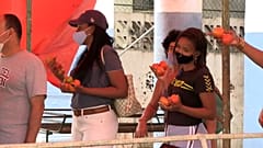Un grupo de persnoas hacen cola para comprar pan con tomates en las manos 