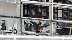 In this March 23, 2016 file photo, an arrivals and departure board is seen behind blown out windows at Zaventem Airport in Brussels.