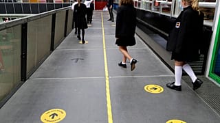 Pupils follow social distancing signs as they walk along a school corridor