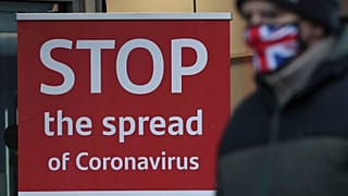 Un hombre con mascarilla pasa ante un cartel "Detener la propagación de coronavirus" en Glasgow