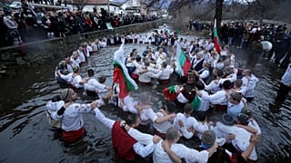 Dozens of citizens of the mountain town of Kalofer, in central Bulgaria, clad in traditional dresses stand in the icy Tundzha River