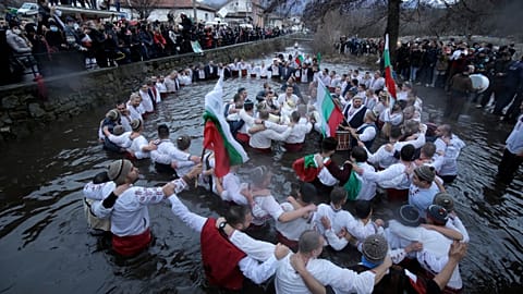 Dozens of citizens of the mountain town of Kalofer, in central Bulgaria, clad in traditional dresses stand in the icy Tundzha River