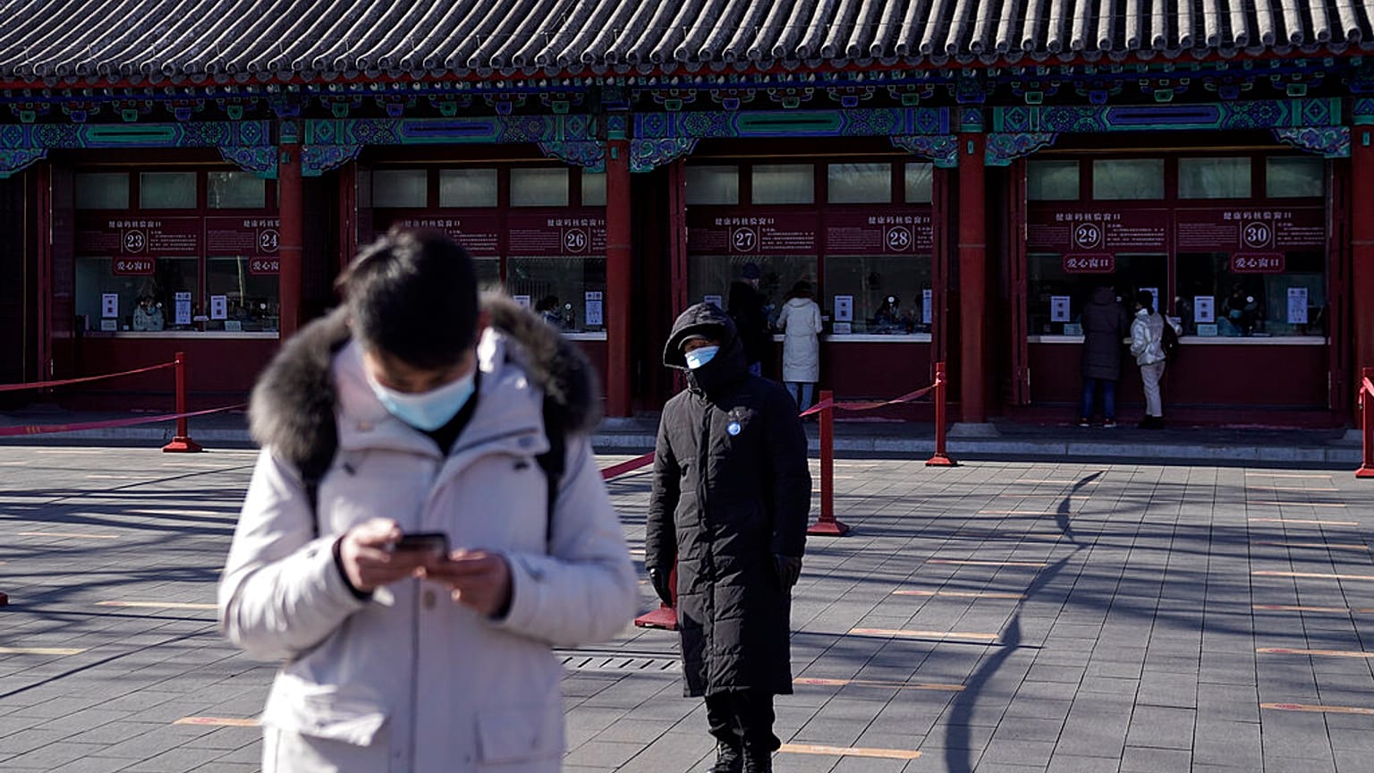 A man wearing a face mask to help curb the spread of the coronavirus browses his smartphone as a masked security guard stands near the quiet ticket counters in Beijing. 