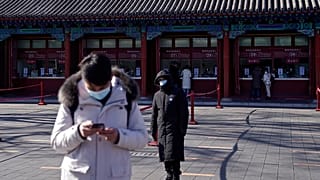 A man wearing a face mask to help curb the spread of the coronavirus browses his smartphone as a masked security guard stands near the quiet ticket counters in Beijing. 