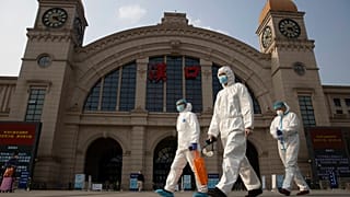 Arbeiter in Schutzanzügen passieren den Bahnhof Hankou (Wuhan) in der zentralchinesischen Provinz, 7.4.2020 Hubei, am Tag vor der Wiederaufnahme des Verkehrs,
