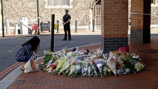 A woman reacts after placing flowers by a police cordon near the scene of a fatal multiple stabbing attack at the Forbury Gardens park, in Reading, England, June 23, 2020.