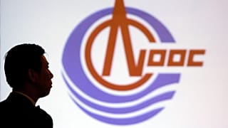 FILE - A man stands in front of the screen featuring logo of CNOOC Limited in Hong Kong, March 29, 2005