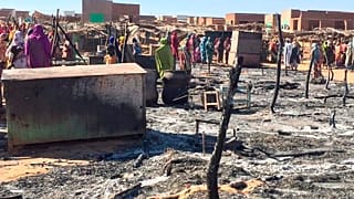 In this Dec. 29, 2019 file photo, residents of a refugee camp gather around the burned remains of makeshift structures, in Genena, Sudan.