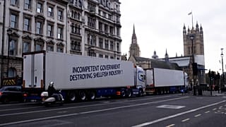 Lorry with ‘Incompetent government destroying shellfish industry’ waiting at a red light with Westminster in the background