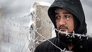 A migrant stands next to a fence during snowfall at the Lipa camp, outside Bihac, Bosnia, Friday, Jan. 8, 2021.