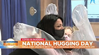 Two people hug through a plastic hugging curtain