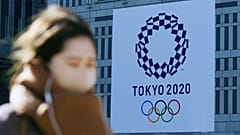 A woman wearing a protective mask to help curb the spread of the coronavirus walks near a banner of the Tokyo 2020 Olympics in Tokyo Tuesday, Jan. 19, 2021.