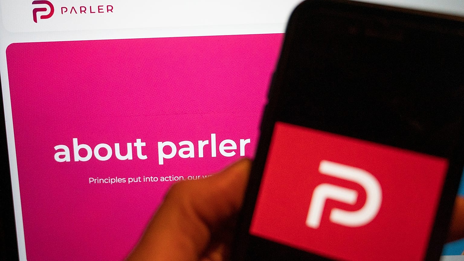 The logo of the social media platform Parler is displayed in Berlin, Jan. 10, 2021. In the background on a screen is the platform's website.