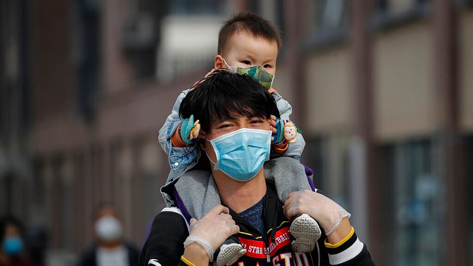 A man carries a toddler on his shoulders as both wear protective face masks to help prevent the coronavirus outbreak walk on a street in Beijing