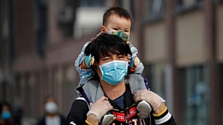A man carries a toddler on his shoulders as both wear protective face masks to help prevent the coronavirus outbreak walk on a street in Beijing