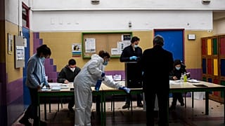 An employee wearing a protective suit cleans as people vote for the Portuguese presidential election