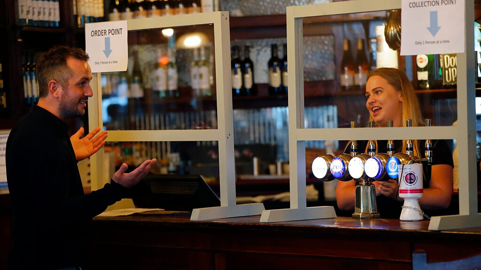 A man orders beer behind a safety screen at the Forester pub in London, Saturday, July 4, 2020