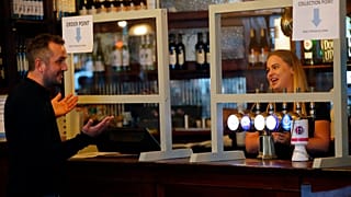 A man orders beer behind a safety screen at the Forester pub in London, Saturday, July 4, 2020