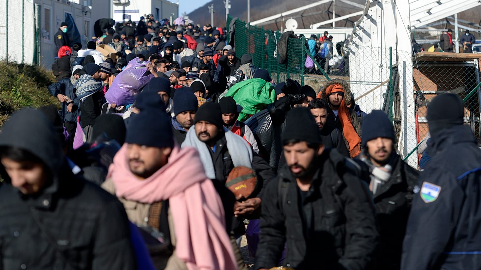 Police officers stand by migrants as they leave to be relocated from the Lipa camp northwestern Bosnia, near the border with Croatia, Bosnia, Tuesday, Dec. 29, 2020. 