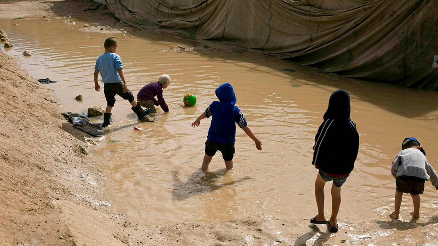 In this March 31, 2019 file photo, children play in a mud puddle in the section for foreign families at Al-Hol camp in Hasakeh province, Syria.