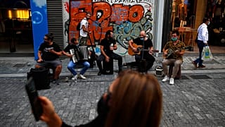 Musicians wearing face masks to prevent the spread of the coronavirus, perform as a woman records a video with her cellphone on Ermou Street,