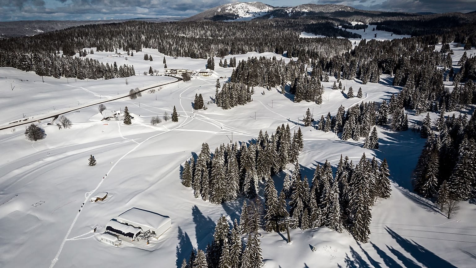 En bas, à gauche, une remontée de la station de Dôle en Suisse. Devant celle-ci, le parking de celle-ci en France, sous la neige le 26 janvier 2021
