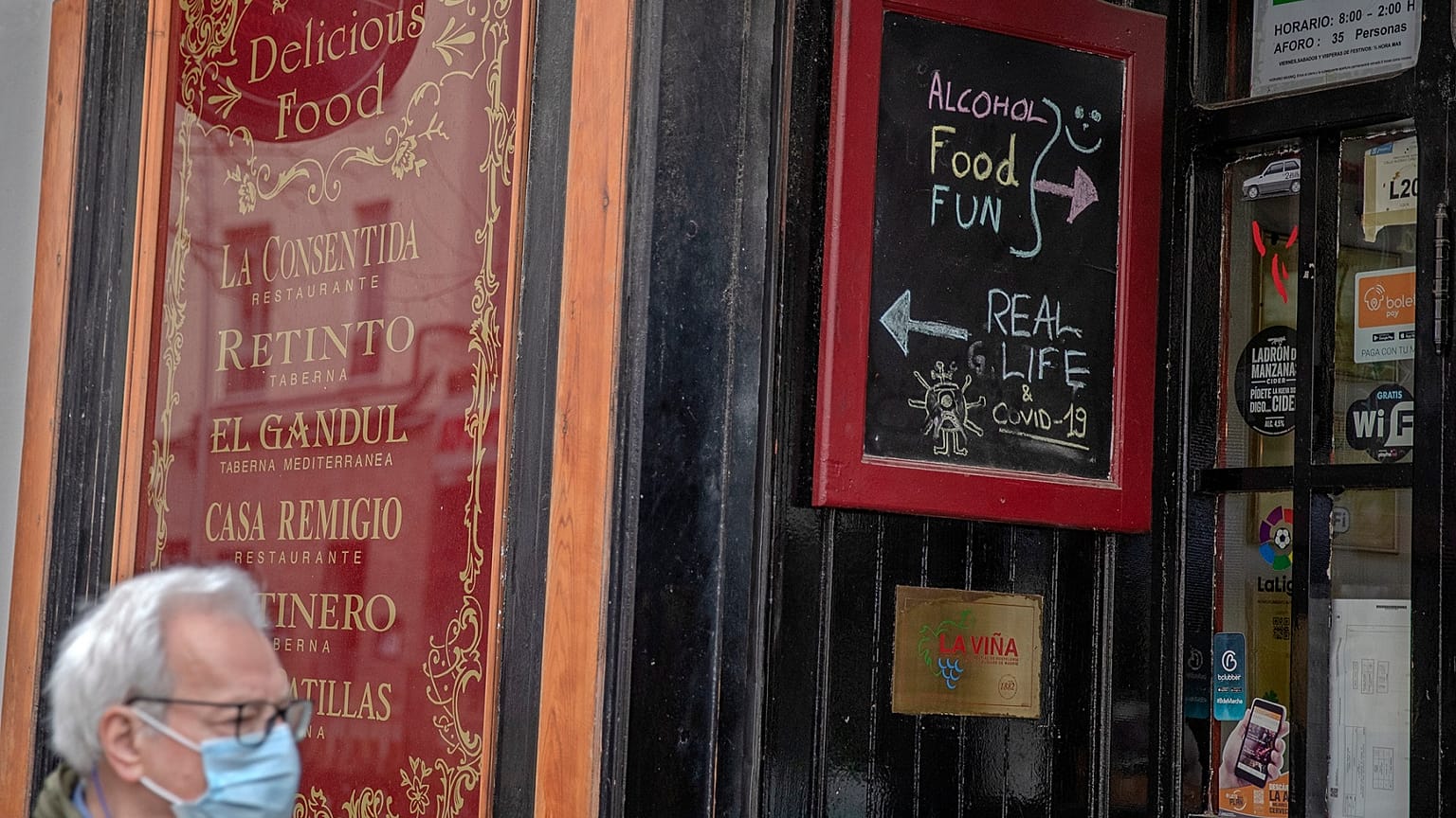 Un hombre con mascarilla pasa por delante de un establecimiento de bebidas abierto.