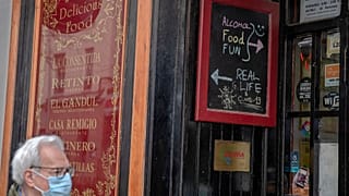 Un hombre con mascarilla pasa por delante de un establecimiento de bebidas abierto.