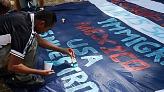 A Central American migrant paints a banner with messages in support of a migrant caravan trying to reach the US at Tecun Uman, Guatemala on the Mexican border, Jan. 22, 2020.