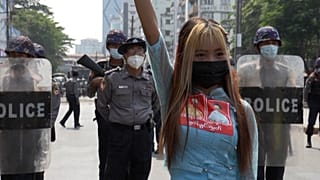 Protester posing for a photo in front of riot police line while holding a three-finger salute.