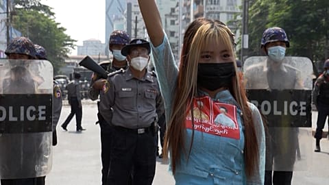 Protester posing for a photo in front of riot police line while holding a three-finger salute.
